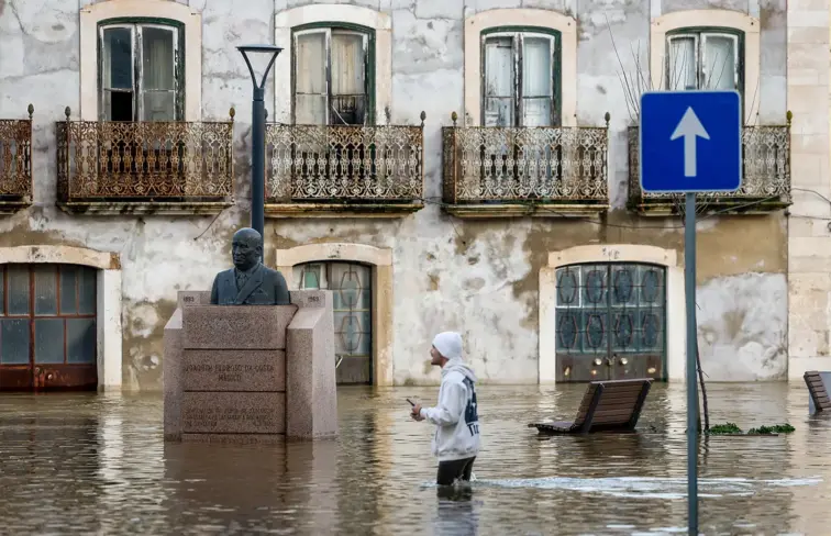 Uma estrada em Santarém inundada pela subida da Ribeira de Santarém, com uma pessoa a passar na estrada e com a água acima dos joelhos.